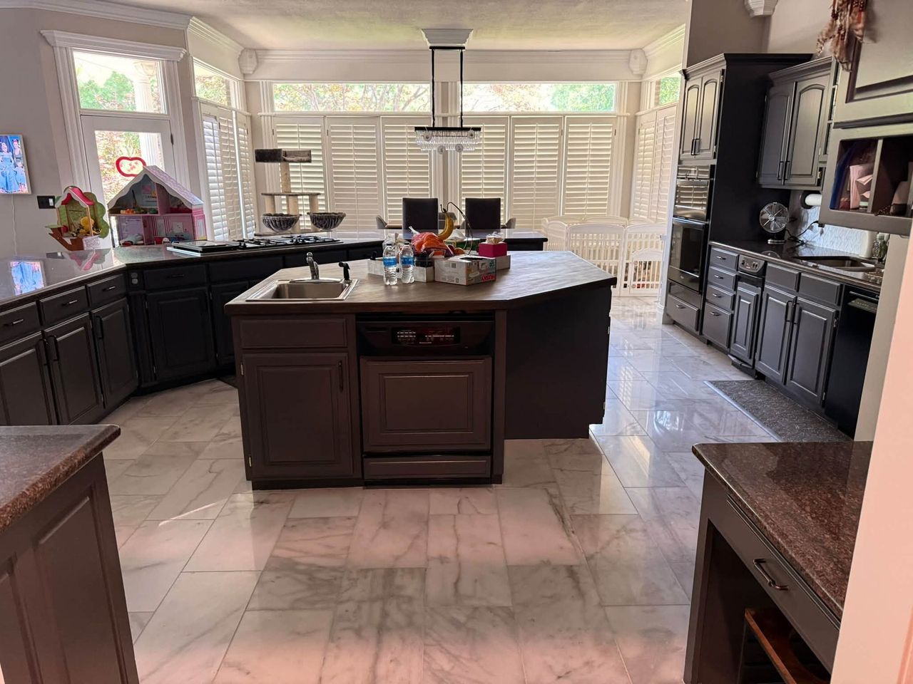 Kitchen with a large island, dark cabinets and polished marble tile floor