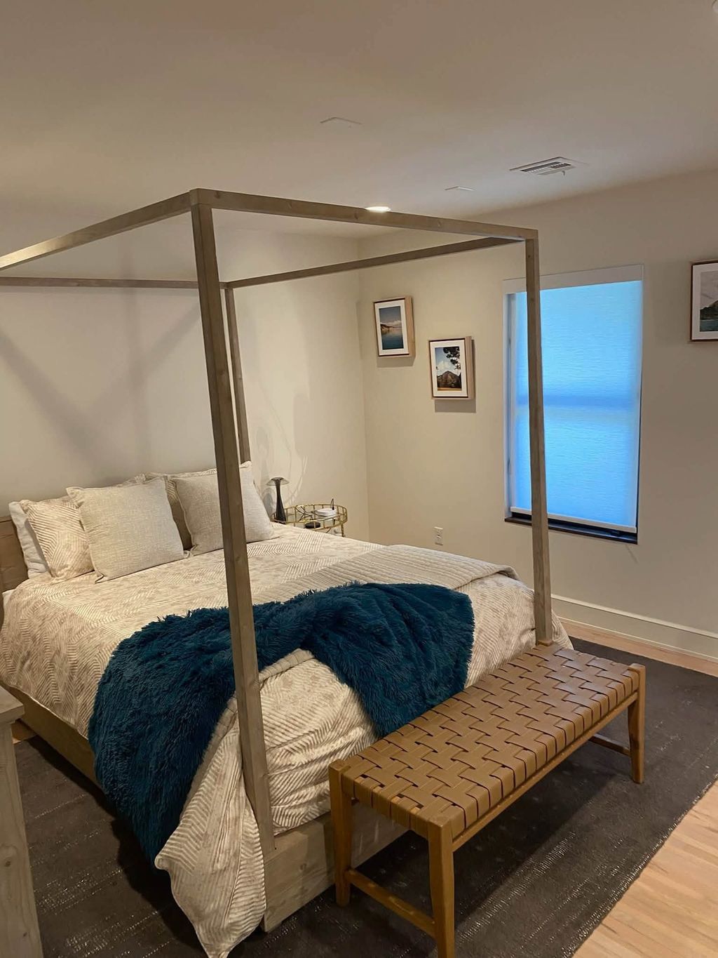 Bedroom with a wooden canopy bed, neutral bedding and a woven bench